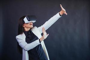 Happy woman on a black background in the studio gets the experience of using VR-glasses virtual reality headset. photo