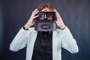 Happy woman on a black background in the studio gets the experience of using VR-glasses virtual reality headset. photo