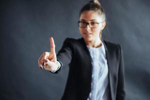 Happy business woman shows finger up, standing on a black background in the studio, friendly, smiling, focus on hand. photo
