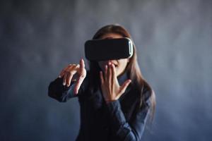 Happy woman on a black background in the studio gets the experience of using VR-glasses virtual reality headset. photo