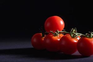 Branch of red organic tomatoes on a black background. photo