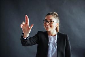 mujer de negocios feliz muestra el dedo hacia arriba, de pie sobre un fondo negro en el estudio, amigable, sonriente, enfocada en la mano. foto