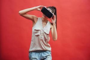 A young woman with a VR device on a red background in studio photo