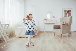 Very beautiful blonde charming little girl standing in the bright interior of the house, in full view photo