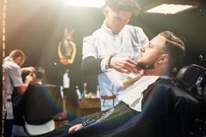 el barbero en el proceso de cortar la barba de las cortadoras eléctricas del cliente en la barbería. foto