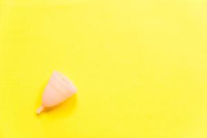 Simply minimal design pink menstrual cup Isolated on yellow background. Woman modern alternative eco gynecological hygiene in menstruation period. Container for blood. Flat lay top view, copy space photo