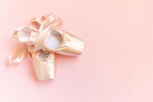 New pastel beige ballet shoes with satin ribbon isolated on pink background. Ballerina classical pointe shoes for dance training. Ballet school concept. Top view flat lay, copy space photo