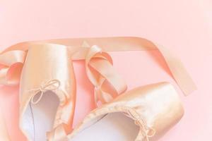 New pastel beige ballet shoes with satin ribbon isolated on pink background. Ballerina classical pointe shoes for dance training. Ballet school concept. Top view flat lay, copy space photo