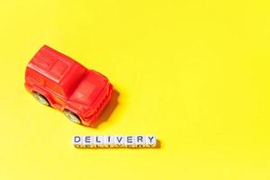 Simply design red toy car and inscription DELIVERY word isolated on yellow colorful background. Internet shopping online purchase e-commerce packages delivery service concept Copy space photo