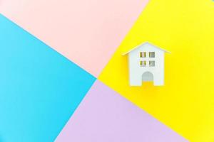 Simply design miniature white toy house isolated on blue yellow pink purple pastel colorful trendy geometric background Mortgage property insurance dream home concept. Flat lay top view copy space. photo