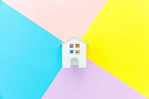 Simply design miniature white toy house isolated on blue yellow pink purple pastel colorful trendy geometric background Mortgage property insurance dream home concept. Flat lay top view copy space. photo