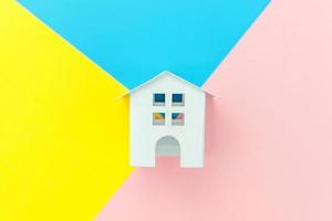 Simply design with miniature white toy house isolated on blue yellow pink pastel colorful trendy geometric background Mortgage property insurance dream home concept. Flat lay top view copy space. photo