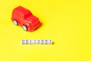 Simply design red toy car and inscription DELIVERY word isolated on yellow colorful background. Internet shopping online purchase e-commerce packages delivery service concept Copy space photo