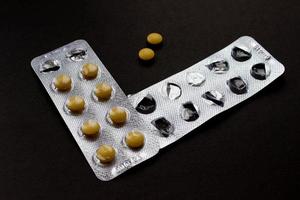 pastillas en un blister, un blister vacío y dos pastillas por separado en un fondo negro foto
