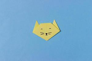 la cabeza del gato está doblada de papel amarillo en la técnica del origami con ojos, nariz y bigote pintados. en medio del fondo azul. foto