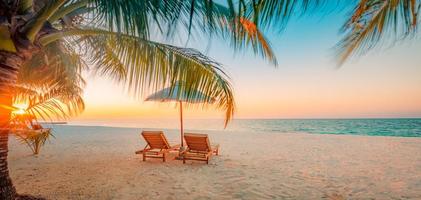 Panoramic tropical beach sunset rays, two sun beds, loungers, umbrella under palm tree. White sand, sea shore horizon, colorful twilight sky, calm relax banner. Inspirational beach resort hotel photo