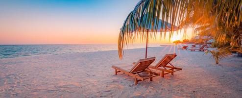 Panoramic tropical beach sunset rays, two sun beds, loungers, umbrella under palm tree. White sand, sea shore horizon, colorful twilight sky, calm relax banner. Inspirational beach resort hotel photo