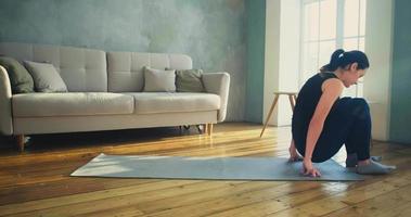 mulher com rabo de cavalo em roupas esportivas pretas deita-se no tapete para fazer exercícios esportivos contra o sofá na sala de estar em câmera lenta video
