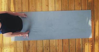 Tranquil young woman in comfortable sportswear does crunches and leg lifts lying on grey mat in room upper view slow motion video