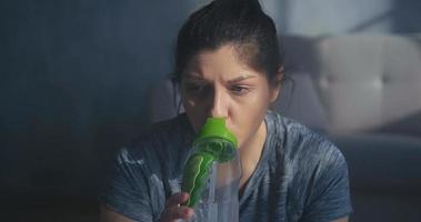 senhora atraente vestindo camiseta cinza bebe água da garrafa após treinamento intensivo na sala de estar vista de perto em câmera lenta
