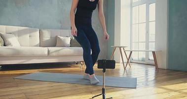 joven blogger de fitness sintoniza el teléfono y muestra abdominales con levantamiento de piernas a sus seguidores en la sala de estar durante la cuarentena en cámara lenta video