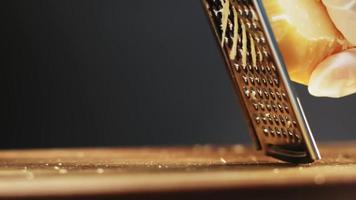 Person in gloves grates delicatessen hard cheese lump for traditional pasta on wooden cutting board extreme closeup slow motion video