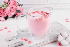 Pink matcha with rose petals on white background. Transparent cup with trendy vegan whipped tea. photo