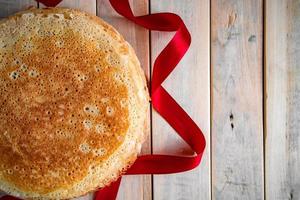 Traditional Russian thin pancakes closeup on a light wooden background and a red ribbon. photo