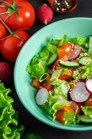 Fresh vegetable salad in a ceramic bowl on gray background. Seasonal summer dish of tomatoes, cucumbers and radishes.