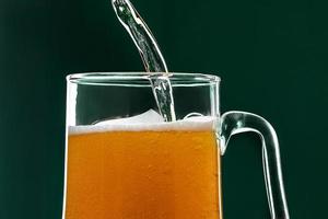 la cerveza se vierte en una taza sobre un fondo verde. foto