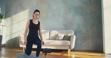 Graceful woman trainer does dynamic lunges shooting videoblog with smartphone in living room during covid quarantine slow motion video