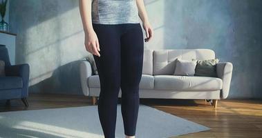Brunette woman in tracksuit stands on digital scales becoming sad of weight at sofa and designed wallpapers slow motion closeup video