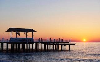 gazebo on the wooden pier into the sea with the sun at sunset photo