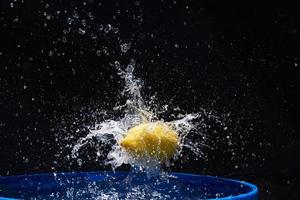 Yellow lemon falling in the blue water on a black background photo