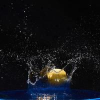 Yellow lemon falling in the blue water on a black background photo