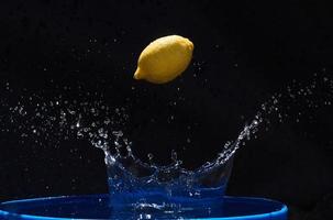 Juicy yellow lemon falls in water on a black background photo