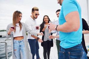 Portrait of a group of young people sitting on the edge of the pier, outdoors in nature. Friends enjoying a game on the lake. photo