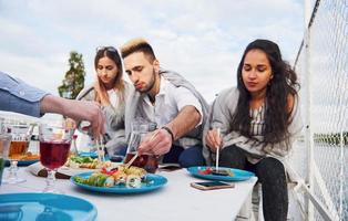 Happy young friends were sitting at a table and having a picnic outdoors photo