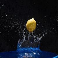 jugoso limón amarillo cae en agua sobre un fondo negro foto