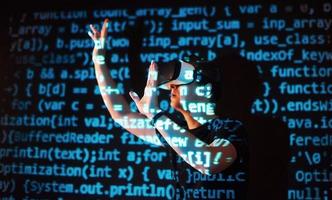 Double exposure of a caucasian man and Virtual reality headset is presumably a gamer or a hacker cracking the code into a secure network or server, with lines of code photo