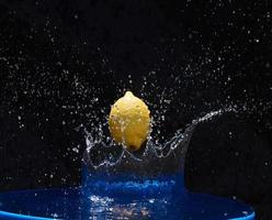 Juicy yellow lemon falls in water on a black background photo