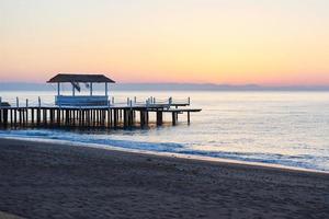gazebo on the wooden pier into the sea with the sun at sunset photo