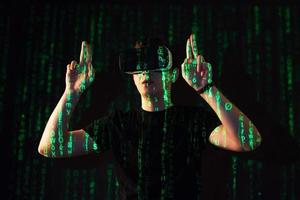 Double exposure of a caucasian man and Virtual reality headset is presumably a gamer or a hacker cracking the code into a secure network or server, with lines of code photo