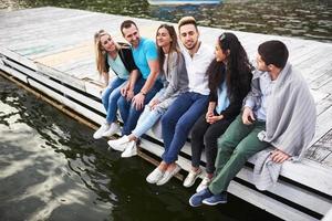 Portrait of happy young friends sitting on a pier at the lake photo