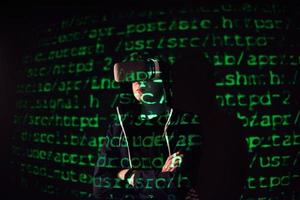 Double exposure of a caucasian man and Virtual reality headset is presumably a gamer or a hacker cracking the code into a secure network or server, with lines of code