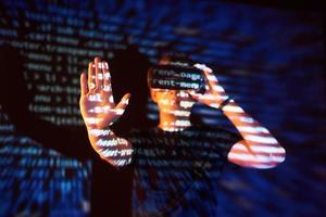 Double exposure of a caucasian man and Virtual reality headset is presumably a gamer or a hacker cracking the code into a secure network or server, with lines of code photo