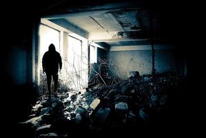 Black human silhouette in a doorway. Human silhouette in an abandoned and ruined place moving to bright light. photo