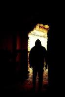 Black human silhouette in a doorway. Human silhouette in an abandoned and ruined place moving to bright light. photo