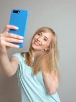 elegante hermosa mujer rubia blogger haciendo selfie con su teléfono inteligente junto a la ventana. tendencia, tecnología, belleza, concepto de moda. foto