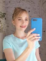 stylish beautiful blonde woman blogger making selfie with her smartphone by the window. Trend, technology, beauty, fashion concept photo